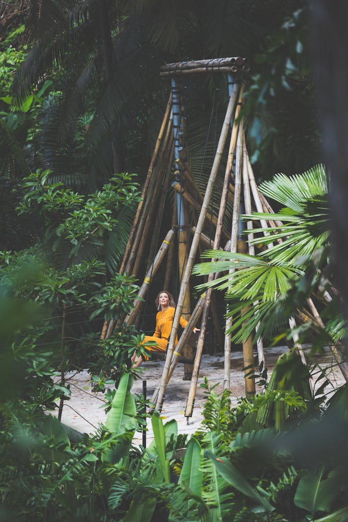 Woman in yellow dress meditating inside bamboo structure surrounded by lush jungle.